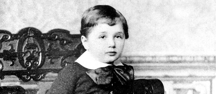 albert einstein as a child standing in front of a wooden chair in a black and white portrait