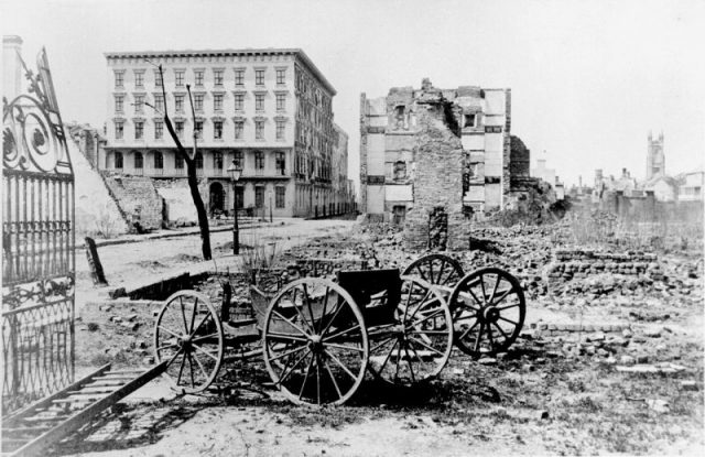 The ruins of Mills House and nearby buildings, Charleston, South Carolina, at end of American Civil War. A shell-damaged carriage and the remains of a brick chimney are in the foreground.