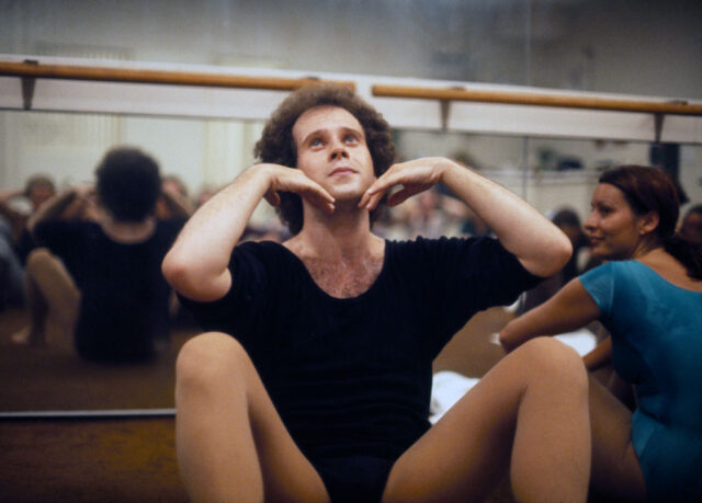 Richard Simmons sitting in a ballet studio with other individuals