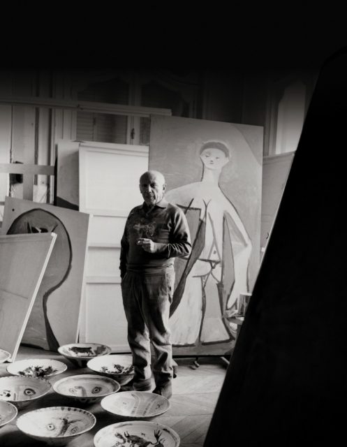 Pablo Picasso standing in the middle of a room filled with pieces of art