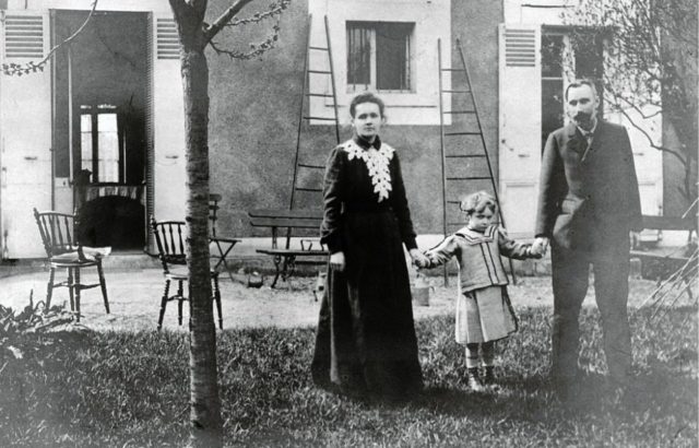 Marie and Pierre Curie holding their daughter's hands in their back garden