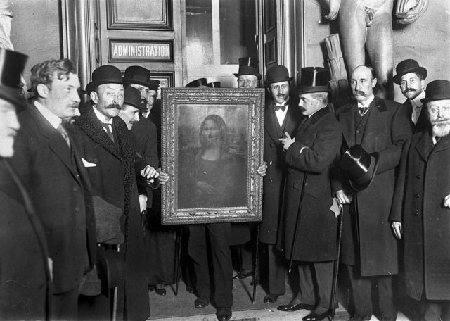 Group of men gather around a man holding the Mona Lisa in a frame after it was returned to the Louvre.