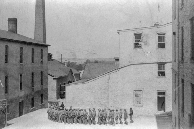Distanced shot of prisoners walking in a line through Leavenworth Penitentiary. 