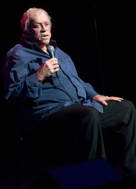 James Gregory sitting in a chair on stage