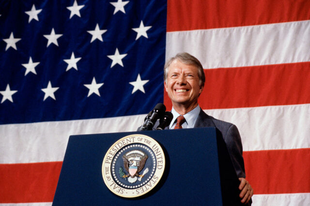 Jimmy Carter standing in front of the American flag, at the presidential podium