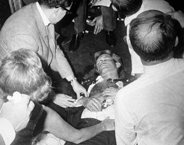 Robert F. Kennedy lying on the ground wounded, people surrounding him.