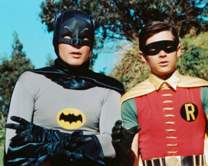 Adam West as Batman and Burt Ward as Robin standing side by side in a scene from the show.