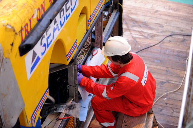 A man in safety gear repairing a machine.