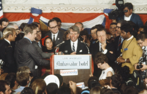 Robert F. Kennedy at a podium, a crowd surrounding him.