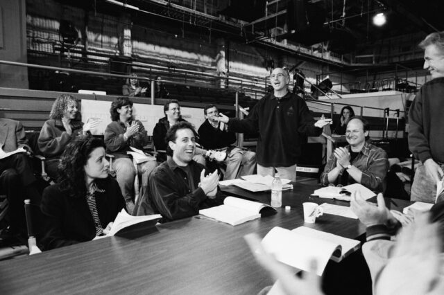 The cast and production of 'Seinfeld' sitting at and around a table.