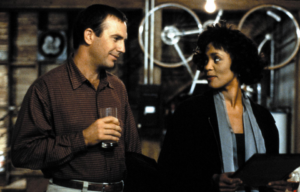 Kevin Costner and Whitney Houston looking at one another.