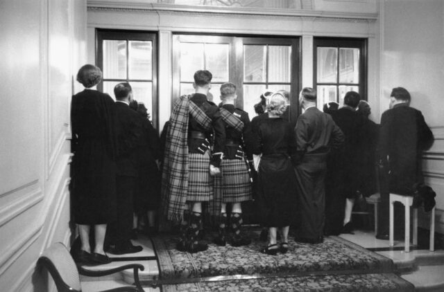 Latecomers to the 1955 Christian Dior fashion shows standing at sets of closed doors, at the end of a hallway