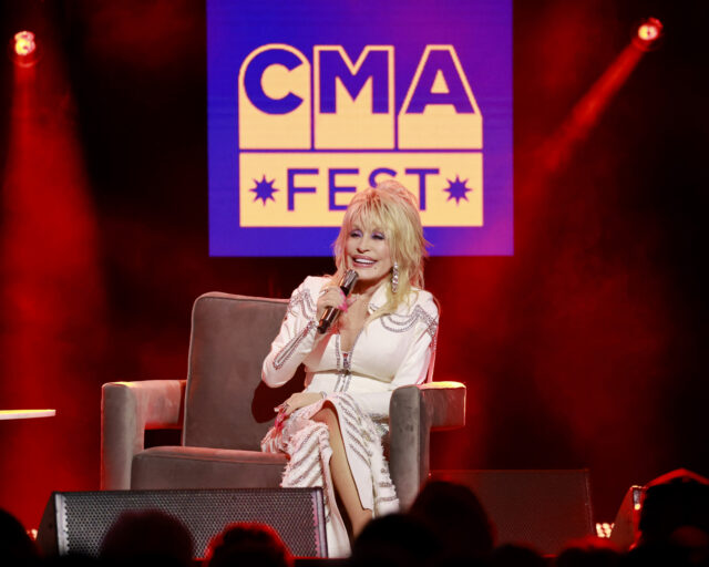 Dolly Parton sitting in a chair holding a microphone.