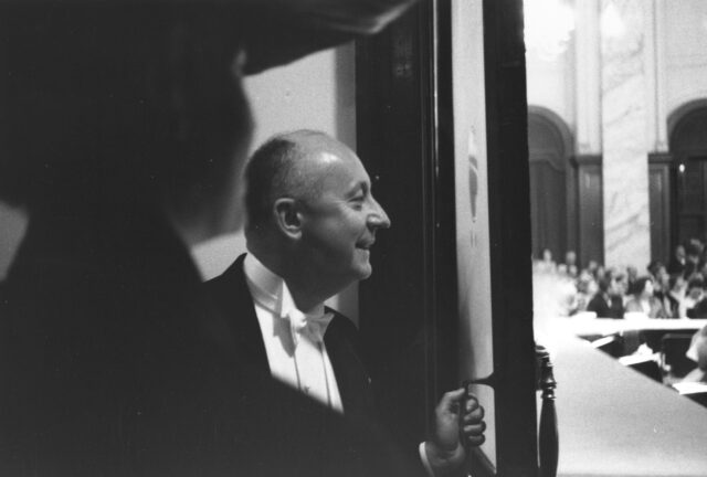 Christian Dior peaking out from behind a door, with a smile on his face