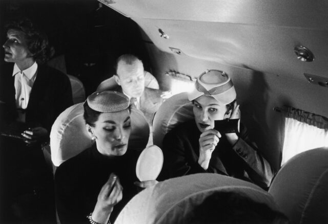 Two women applying their makeup while sitting in airplane seats