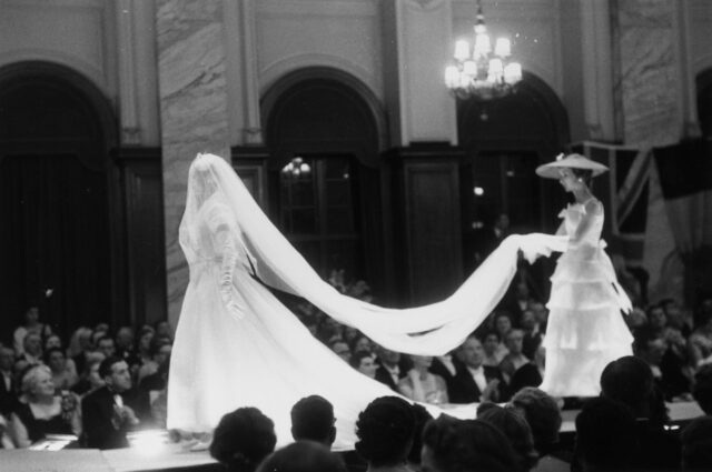 Two models walking down a catwalk as spectators look on