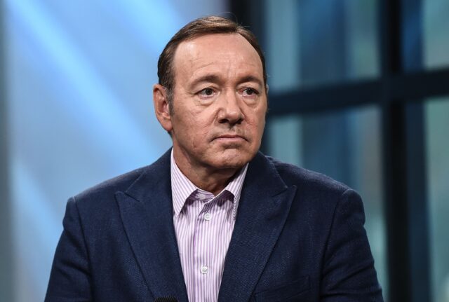 Kevin Spacey sitting in a suit, with a serious expression on his face