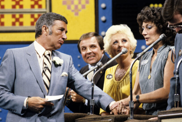 Robert Dawson leaning on a counter, a family of contestants speaking into their microphone.