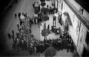 A crowd gathered around a guillotine out front of a building.