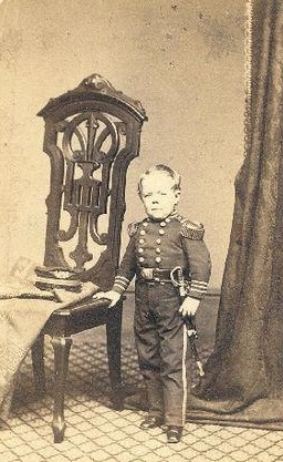 Commodore Nutt standing by a chair.