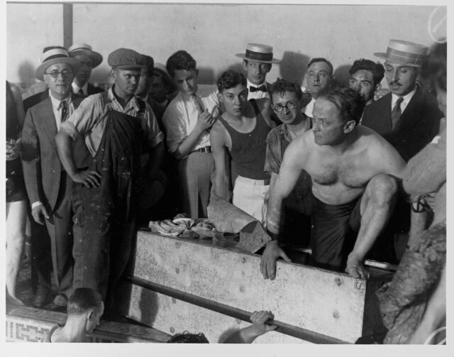 Harry Houdini emerging from a coffin, people surrounding him.