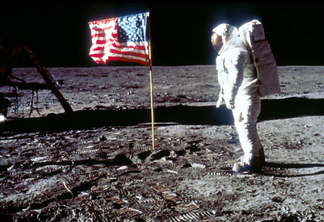 An astronaut on the moon, an American flag posted in its service.