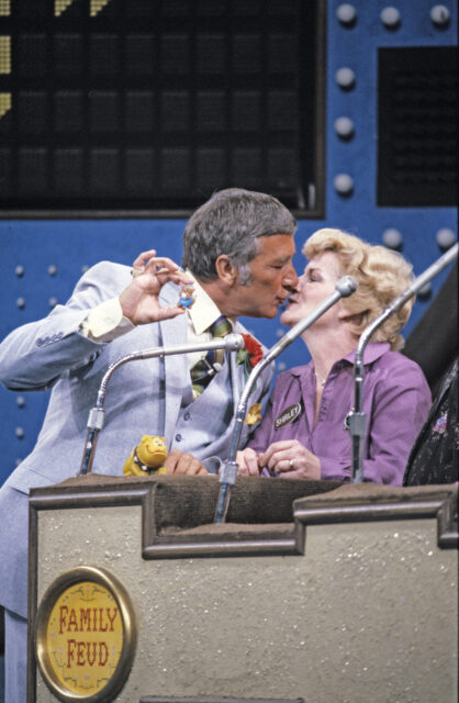 Richard Dawson holds up a figurine while kissing a contestant.