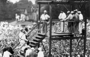 Men walk the stairs of a public hanging execution platform.