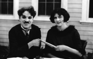 Charlie Chaplin and Lita Grey sitting beside one another and smiling.