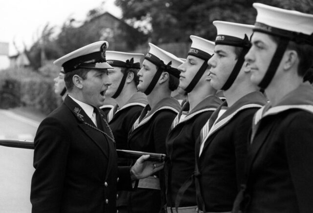 Chief Petty Officer Philip Greenaway giving orders to British Royal Navy sailors who are standing in a row