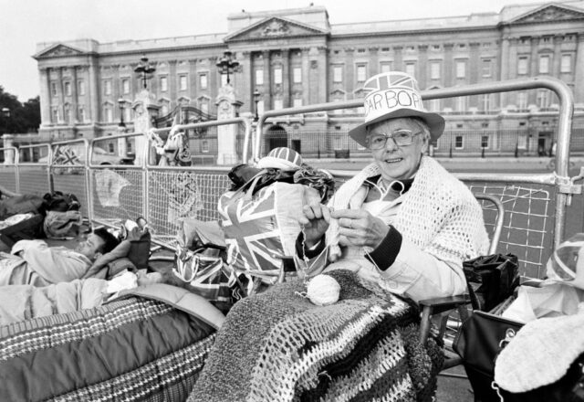 Kathleen Lucus knitting while sitting in front of Buckingham Palace