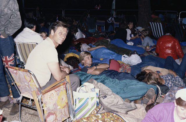 People lying in sleeping bags and a man sitting in a foldable chair