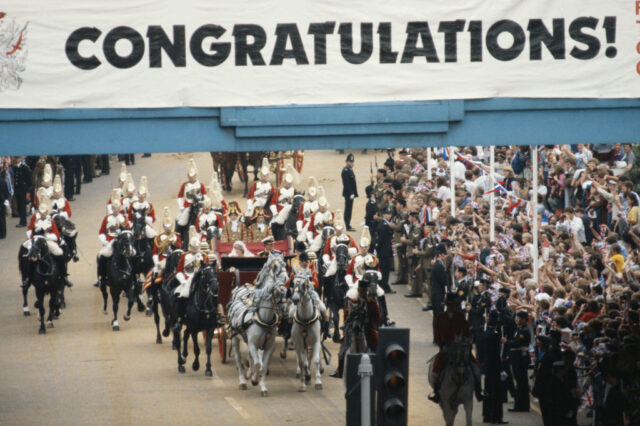 Princess Diana and Prince Charles being transported beneath a sign that reads, "CONGRATULATIONS"