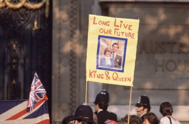 Sign featuring a portrait of Lady Diana Spencer and Prince Charles, held above a crowd of people