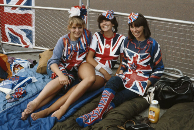 Three women sitting on the ground while wearing clothing decked out in Union Jacks