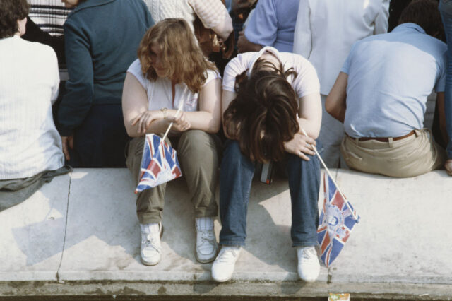 Two girls sitting with their heads toward the ground behind a group of people