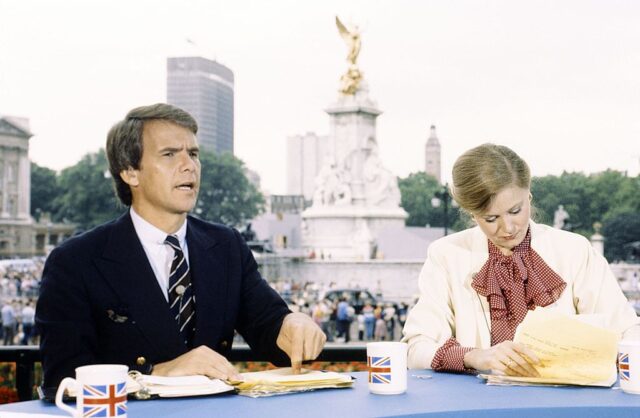 Tom Brokaw and Jane Pauley sitting at a desk outside of Buckingham Palace