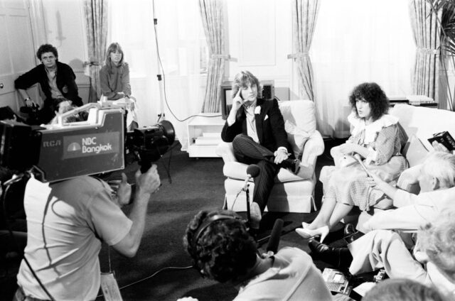 Television crew standing around David and Elizabeth Emanuel, who are sitting on a couch