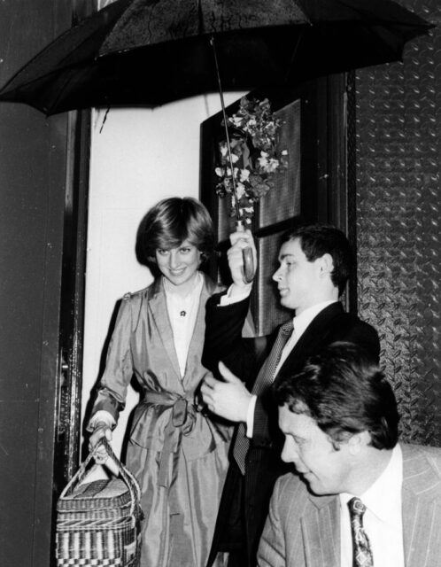 Lady Diana Spencer walking out of a building, while a man stands next to her, holding an umbrella