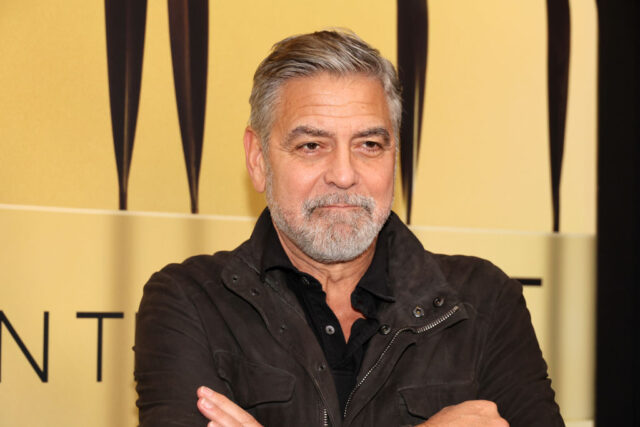 George Clooney standing on a red carpet with his arms crossed in front of him