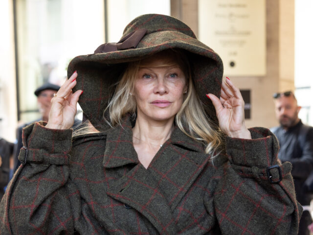 Pamela Anderson holding an oversized hat on her head.