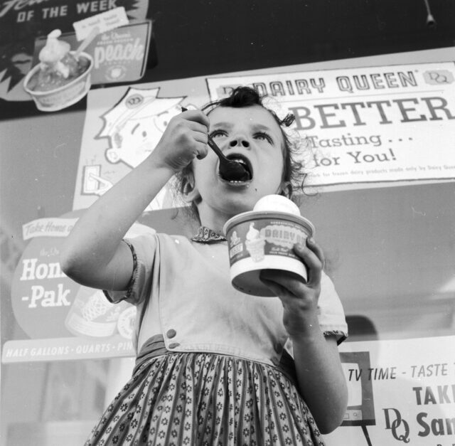 A little girl eating ice cream outside of a Dairy Queen.