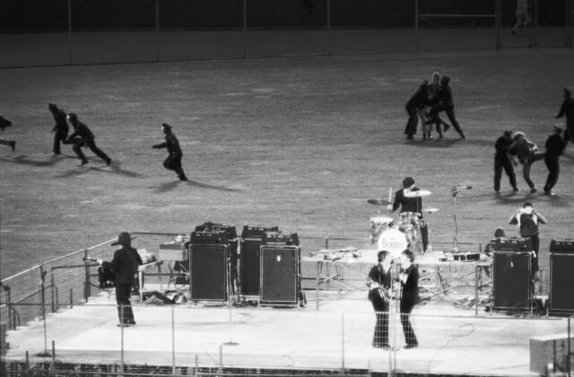 Policemen stopping women from reaching the stage where The Beatles are performing.