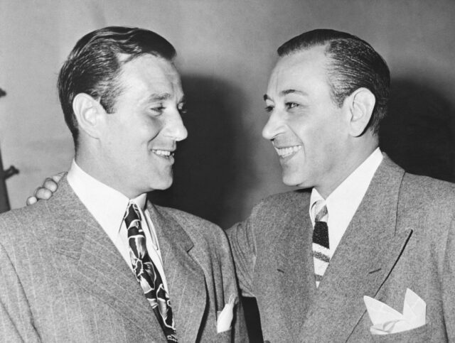 George Raft and Bugsy Siegel smiling at each other.