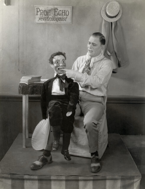 Lon Chaney sitting on a chair with a ventriloquist dummy.