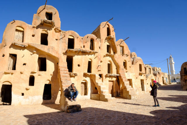 A tiered building in the Tunisian desert, a man sits on the steps.