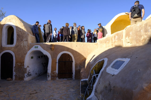 Several people standing atop a row of desert huts.