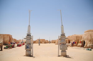 Two 'Star Wars' props standing in the courtyard of desert buildings.