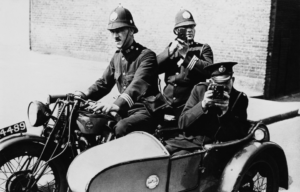 Three police officers in a motorcycle and sidecar, two looking through camera.