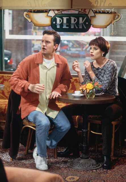 Paget Brewster and Matthew Perry sitting at a cafe table.